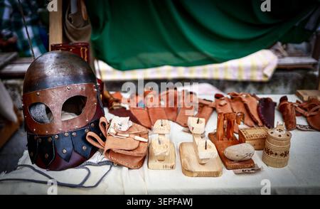 Tallinn, Estonie - 11 juillet 2025 : un casque médiéval, de la maroquinerie et de l'artisanat en bois sont exposés sur une table au marché médiéval des jours Banque D'Images