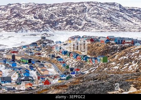 Paysage urbain hivernal de Qaqortoq avec des maisons en bois lumineux, des rues enneigées, un terrain rocheux et des montagnes arctiques spectaculaires, Qaqortoq, Kujalleq Banque D'Images