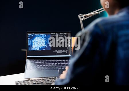 Femme indépendante travaillant sur son ordinateur portable à un bureau axé sur le codage ; afro-américaine utilisant son ordinateur personnel pour surveiller le réseau neuronal, montrant un logiciel d'interface futuriste. Banque D'Images