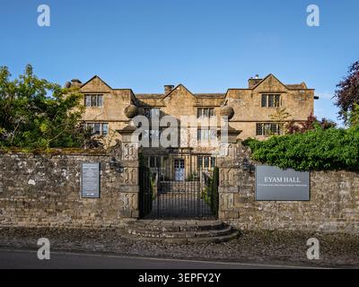 Large vue horizontale du bord de la route montrant le mur périmétrique en pierre, les piliers de la porte et les portes d'entrée menant au parc d'Eyam Hall Banque D'Images