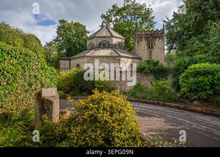 Vue panoramique horizontale sur l'église historique St Martin encadrée par un poteau de pierre et des buissons verdoyants de jardin à Stoney Middleton Banque D'Images