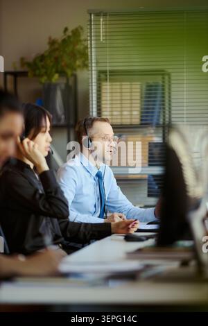 Photo verticale de jeunes adultes travaillant sur des micro-casques/oreillettes au bureau, traitant les appels du service client et les communications professionnelles. Pour le marketing des centres de contacts Banque D'Images