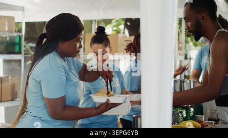 Jeunes travailleurs caritatifs, servant des aliments frais à ceux qui en ont besoin, offrant soutien et secours aux sans-abri et aux réfugiés, aux pauvres et aux personnes affamées recevant des repas gratuits à la banque alimentaire extérieure. Banque D'Images