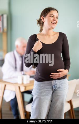 Heureuse jeune femme enceinte patiente quittant le cabinet médical après rendez-vous chez le médecin dans le centre médical Banque D'Images