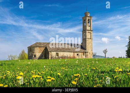 Église en pierre et pissenlits fleuris sous un beau ciel à Prunetto, Piémont, Italie Banque D'Images