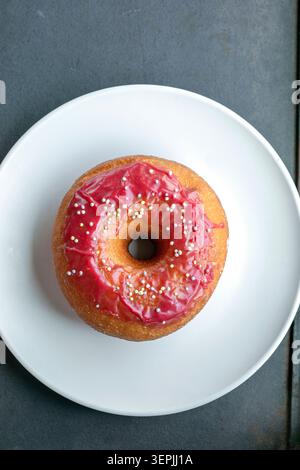 Beignet émaillé rose simple avec des saupoudres sur l'assiette Banque D'Images