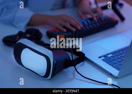Mains tapant sur le clavier avec casque VR de réalité virtuelle et ordinateur portable pour une technologie de jeu immersive Banque D'Images