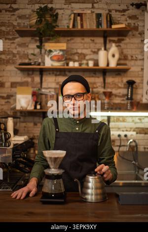 Un jeune barista concentré prépare un café filtre alternatif avec une bouilloire et un goutteur Banque D'Images