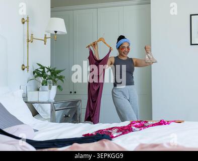 Femme debout près du lit tenant une robe marron et des sandales transparentes, portant des patchs sous les yeux, espace de copie Banque D'Images