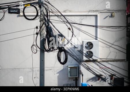 Gros plan d'un poteau électrique avec des fils et des câbles électriques emmêlés projetant des ombres sur un mur de ville Uni, représentant une infrastructure électrique urbaine et Banque D'Images