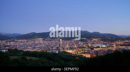 Bilbao la nuit Bilbao paysage urbain mettant en valeur ses bâtiments illuminés et ses structures imposantes contre les montagnes sombres et le ciel crépusculaire, transportant u Banque D'Images