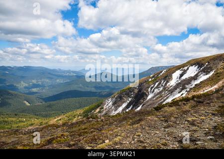 Crête de montagne rocheuse avec de la neige et des vallées vertes sous le ciel bleu avec des nuages. Banque D'Images