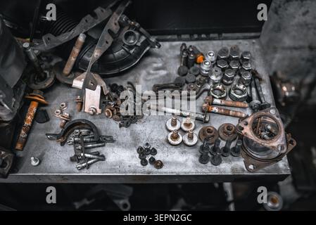 Une collection de divers composants et quincaillerie de voiture usagés, y compris des boulons, des écrous et des supports, dispersés sur une surface métallique usée Banque D'Images