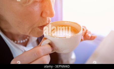 Gros plan de femme mature avec Latte au Café. Femme âgée buvant calmement du café mousseux pendant la matinée. Fermer vue d'une femme senior savourant son Latte Banque D'Images