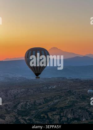Une montgolfière flotte gracieusement au-dessus des paysages magnifiques de la Cappadoce au lever du soleil. Banque D'Images