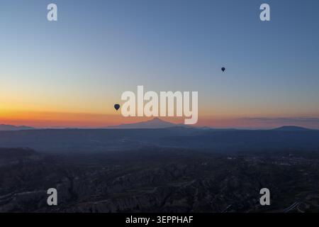 Cette superbe image capture des montgolfières survolant le paysage unique de la Cappadoce au lever du soleil. Banque D'Images