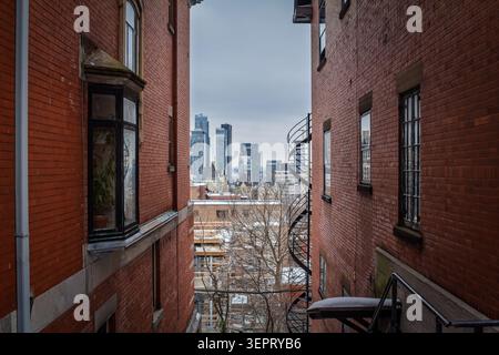 Vue sur les gratte-ciel de Montréal et le quartier des affaires du centre-ville entre les bâtiments résidentiels en briques rouges, montrant les logements urbains, les tours d'affaires et la densité immobilière Banque D'Images