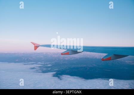 Vue aérienne de voyage de la Nouvelle-Zélande depuis le siège de fenêtre de l'avion de l'aile sur une épaisse couche de nuages blancs et des crêtes sous le ciel crépusculaire bleu avec une petite lune. Banque D'Images