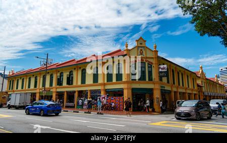 Boutiques historiques colorées dans le quartier patrimonial Kampong Glam de Singapour sous un ciel bleu vif avec circulation routière et voitures qui passent. Banque D'Images