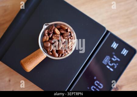 Grains de café torréfiés dans une cuillère à mesurer sur une échelle noire montrant 15 grammes. Concept de pesée des grains de café, de préparation du café et de recette. Banque D'Images