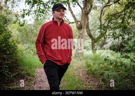 Homme en veste rouge marchant à travers la forêt, profitant de l'activité de plein air Banque D'Images