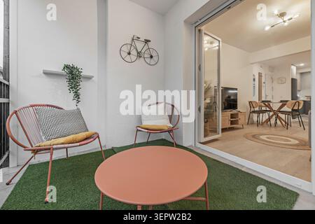 Un balcon-terrasse allongé avec une balustrade en verre trempé, deux chaises longues pliantes, une table basse et un jardin vertical luxuriant de fougères et de pothos Banque D'Images