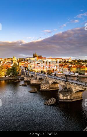 L'aube se lève sur la rivière Vltava, illuminant le pont Charles et l'impressionnant château de Prague. La scène paisible capture la beauté de l'architecture de la vieille ville et des eaux tranquilles. Banque D'Images