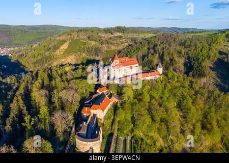 Une vue du ciel sur le château de Pernstejn montre sa structure entourée d'arbres et d'une colline. Le paysage comprend des forêts vertes et un ciel clair. Cette scène capture le design médiéval. Banque D'Images