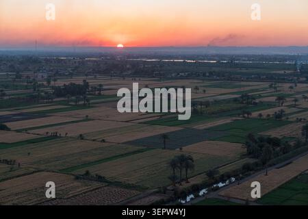 Vue aérienne sur le patchwork agricole de la vallée du Nil au coucher du soleil, Louxor, Egypte. Terres agricoles vertes et dorées avec des palmiers, le Nil et la ville visibles à l'horizon Banque D'Images