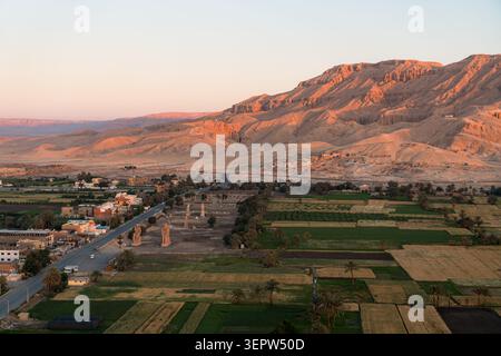 Vue aérienne des Colossi de Memnon émergeant des terres agricoles de la vallée du Nil, avec les montagnes thébaines dramatiques de la Vallée des Rois en arrière-plan. Louxor, Ég Banque D'Images