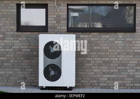Une pompe à chaleur se tient contre un mur de briques d'une maison par une journée froide. Il fonctionne pour fournir le chauffage pour l'intérieur. Les fenêtres voisines montrent la structure de t Banque D'Images