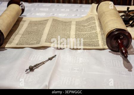 Gros plan à angle élevé d'un rouleau sacré de Torah hébreu manuscrit, partiellement déroulé sur une nappe blanche à côté d'un pointeur de lecture argenté traditionnel Banque D'Images