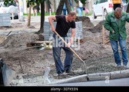 Deux hommes se concentrent sur les travaux routiers, en utilisant des outils pour préparer la rue de la ville pour les réparations. Kiev, Ukraine, 16 juin 2026 Banque D'Images