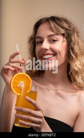 Jeune femme souriante, profitant d'une boisson rafraîchissante à l'orange avec une paille, présentant un mode de vie sain et de la gaieté Banque D'Images