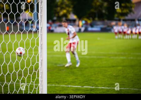 Un joueur de football dans un uniforme blanc frappant un tir de pénalité vers le but pendant un match de football, vu à travers le filet. Banque D'Images