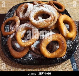 Beignets dorés maison saupoudrés de sucre en poudre sur une assiette noire. Banque D'Images