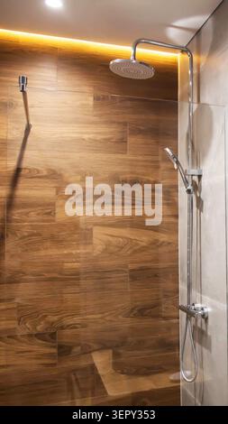 Vue détaillée de la cabine de douche contemporaine. Carreaux élégants à effet de grain de bois riche et contrasté, carreaux muraux neutres légers. Système de douche chromé élégant Banque D'Images