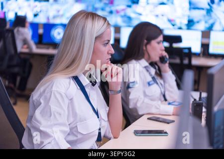 Une rangée de répartiteurs de sécurité féminins professionnels portant des uniformes travaillant à leurs bureaux, répondant aux appels d'urgence et surveillant les écrans d'ordinateur Banque D'Images