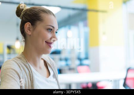 Un portrait en gros plan de profil latéral d'une jeune femme caucasienne joyeuse avec ses cheveux blonds attachés dans un chignon haut soigné. Elle sourit largement, montrant Banque D'Images
