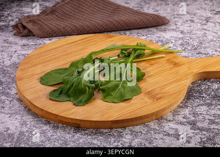 Feuilles de roquette vertes fraîches disposées sur une planche à découper ronde en bois avec une serviette brune à texture gaufrée en arrière-plan, sertie contre une pierre grise sur Banque D'Images