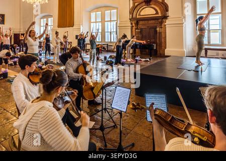 L’ensemble Bella Musica se produit dans la salle de bal de la résidence de l’archevêque (DomQuartier Salzburg), tandis qu’à droite, un professeur de yoga sur le podium fait une pose levant les bras. L’événement « Pop Up Yoga – Mozart Edition » combine musique live et séance de yoga guidée. Salzbourg, Autriche Banque D'Images