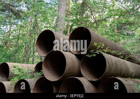 Oléoducs industriels abandonnés laissés dans les bois, concept écologique. Gros tuyaux en métal rouillé empilés dans une forêt verte de gros plan. Banque D'Images