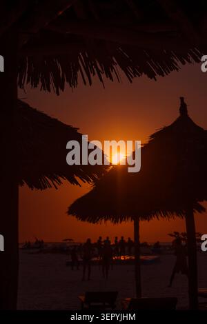 Coucher de soleil doré sur une plage tropicale à Zanzibar avec des silhouettes de parasols de paille traditionnels et des gens. Prise de vue verticale. Banque D'Images