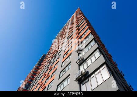 Vue en contre-plongé de la façade d'un immeuble résidentiel moderne en gratte-ciel avec des détails orange et gris devant un ciel bleu clair, concept immobilier Banque D'Images