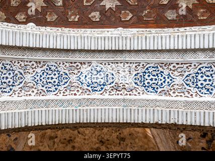 Gros plan d'une arche sculptée avec des motifs arabesques bleus sous un plafond géométrique complexe en marqueterie en bois à l'Alhambra de Grenade, en Espagne Banque D'Images
