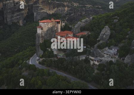 Vue aérienne du monastère Rousanou dans les Météores avec ses toits de tuiles rouges perchés sur un pilier rocheux abrupt entouré d'une forêt dense et verdoyante à Trikala, Banque D'Images