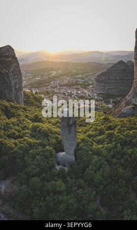 Vue aérienne du pilier rocheux Adrachti s'élevant d'une forêt verte dense avec la ville de Kastraki en arrière-plan pendant le coucher du soleil à Météores, Trikala Banque D'Images