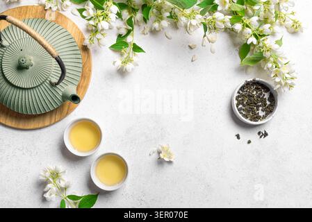 Thé vert au jasmin dans une théière et des tasses à thé sur fond blanc, vue de dessus, espace de copie. Thé naturel au jasmin et fleurs. Banque D'Images