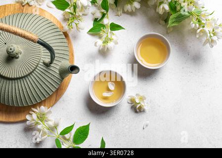 Thé vert japonais au jasmin dans une théière en fonte et des tasses à thé sur fond blanc, vue de dessus, espace de copie. Thé au jasmin naturel et branches florissantes. Banque D'Images