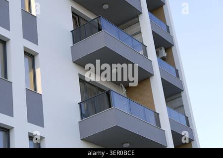 Immeuble résidentiel contemporain avec balcons empilés, balustrades en verre et façades grises, lignes géométriques épurées et symétrie par rapport à un ciel clair, urb Banque D'Images